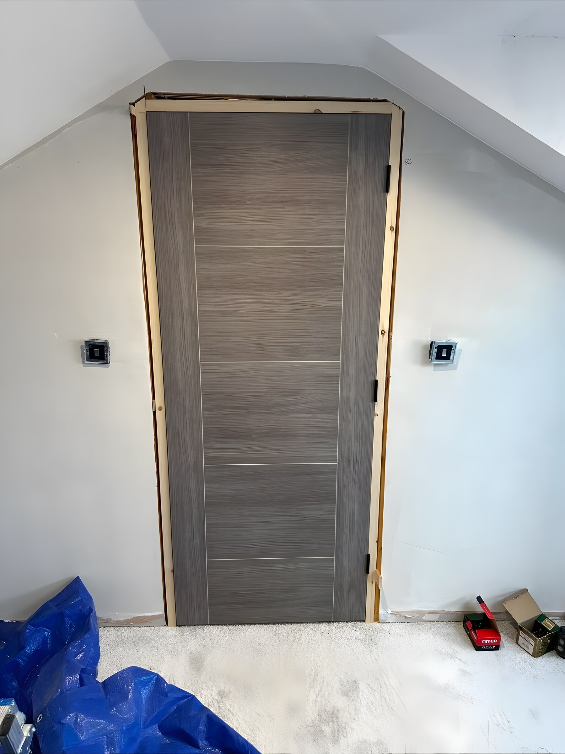 A grey door hung in its lining in a loft room, before the architrave