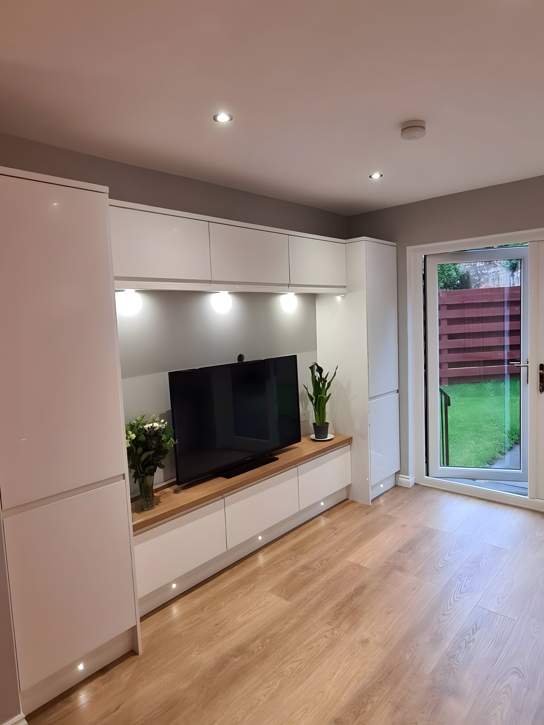 A media wall built in at the end of a kitchen, with an oak shelf