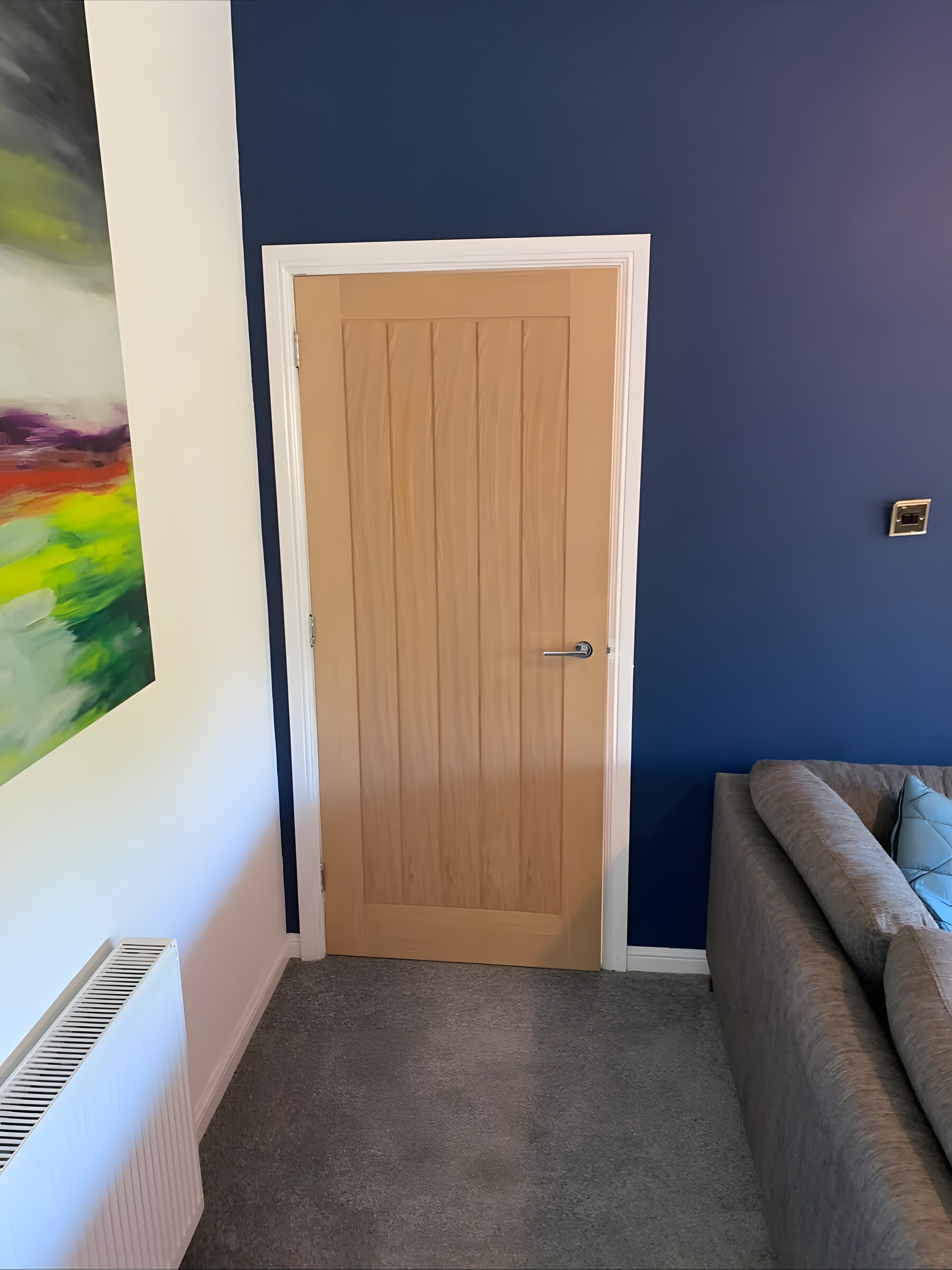 An oak door in a living room, cased in white architrave