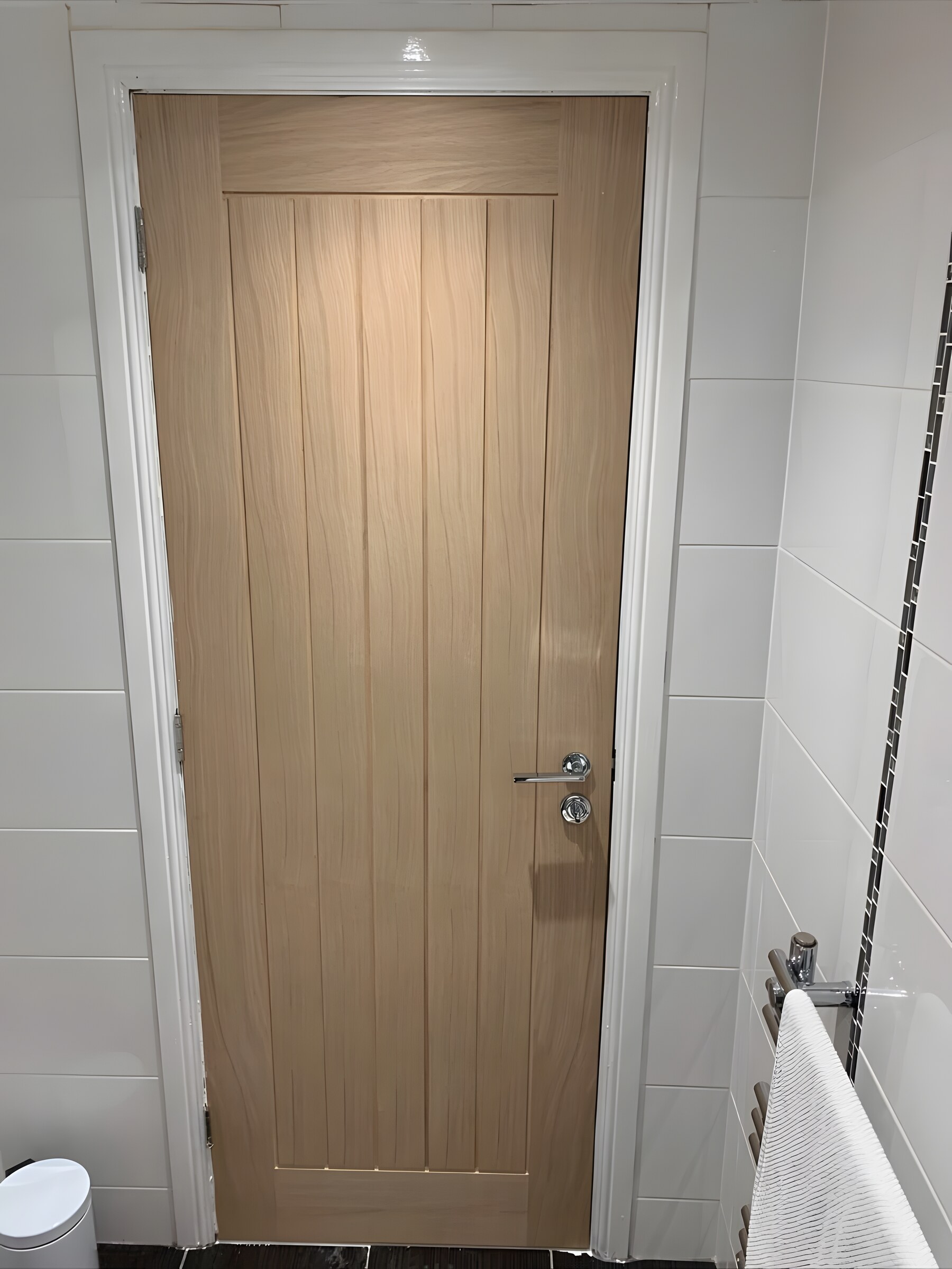 An oak door in a tiled bathroom — lever handle and thumb turn