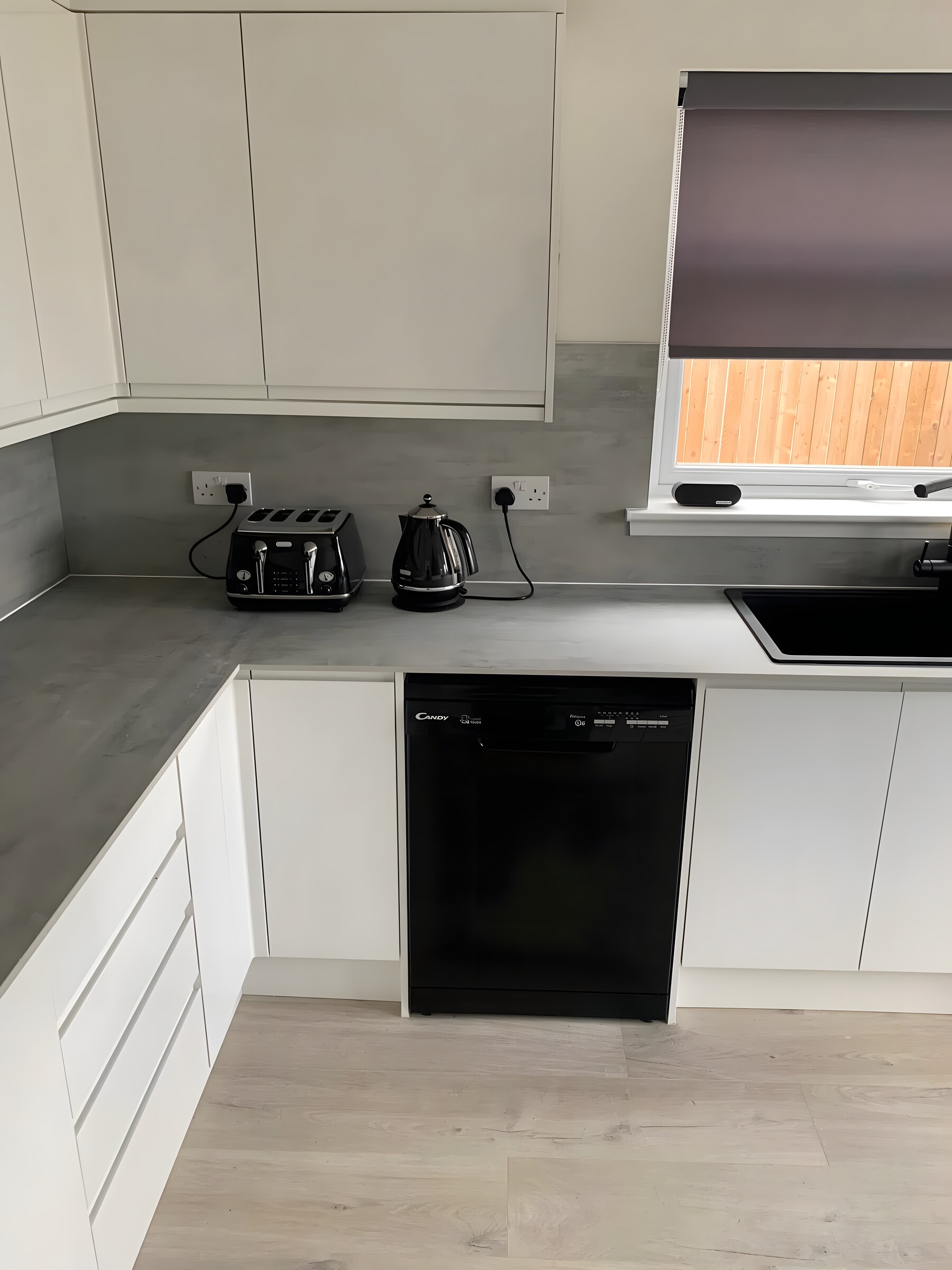 A compact white handleless kitchen, grey worktop
